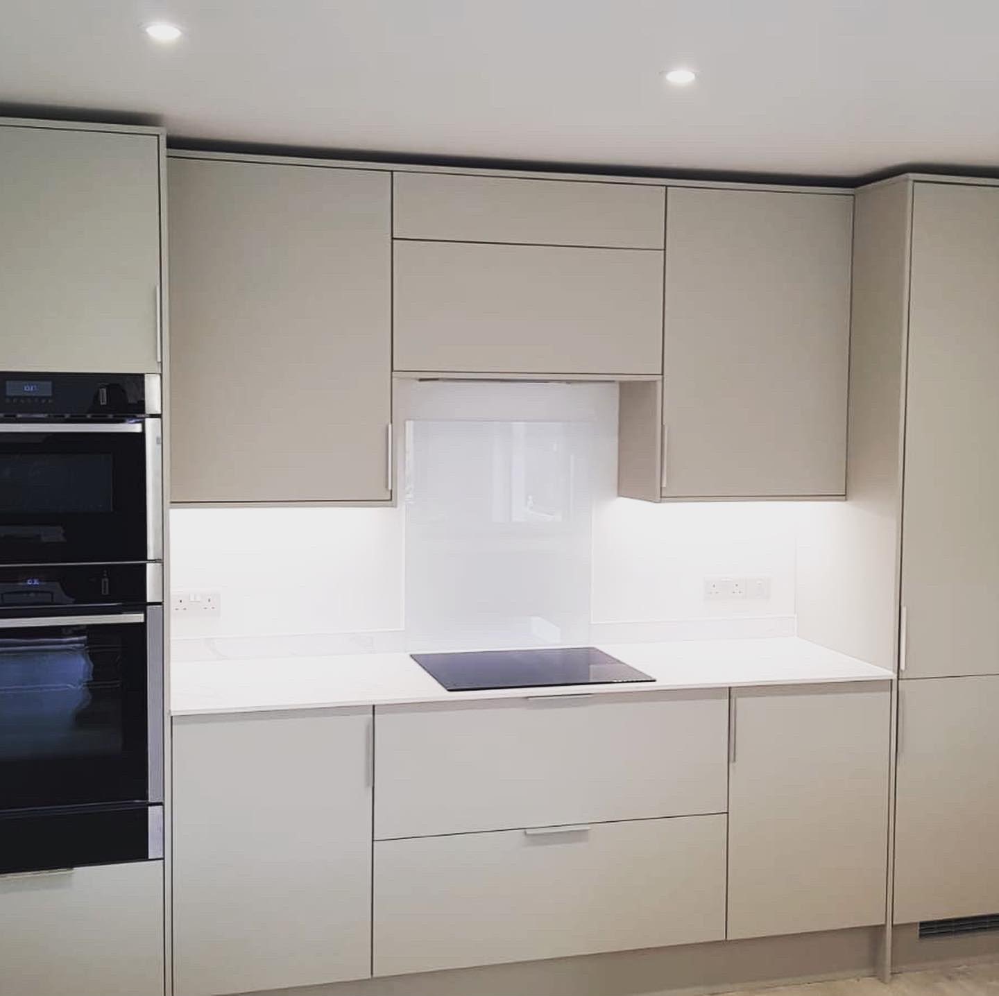 Cashmere handleless kitchen with a glass splashback and built-in double oven