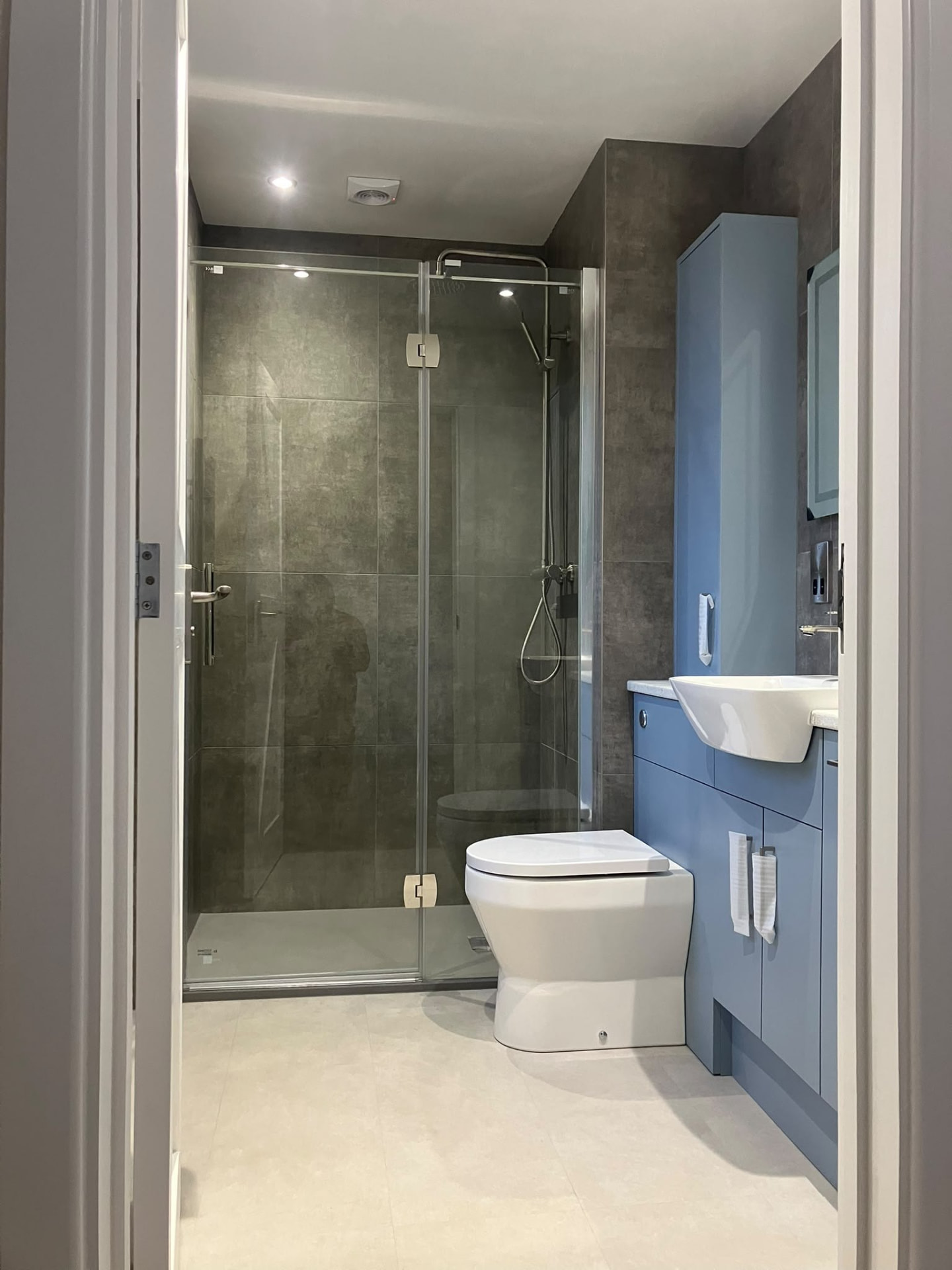 Full view of a completed grey-tiled bathroom with a walk-in glass shower screen