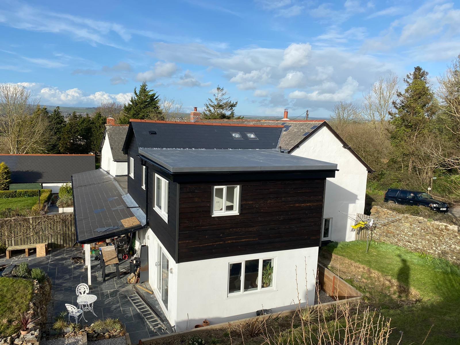 Two-storey black timber-clad extension with a slate roof on a rendered house