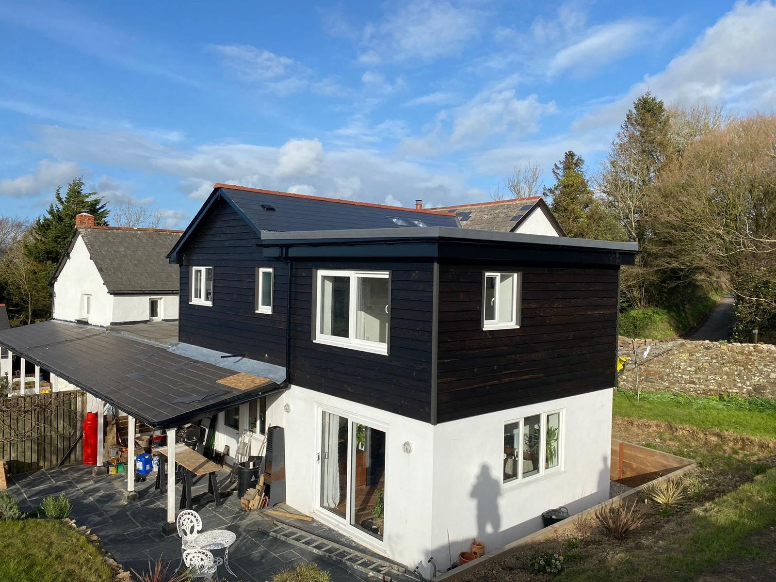 Two-storey extension clad in black timber with a white rendered ground floor and new patio