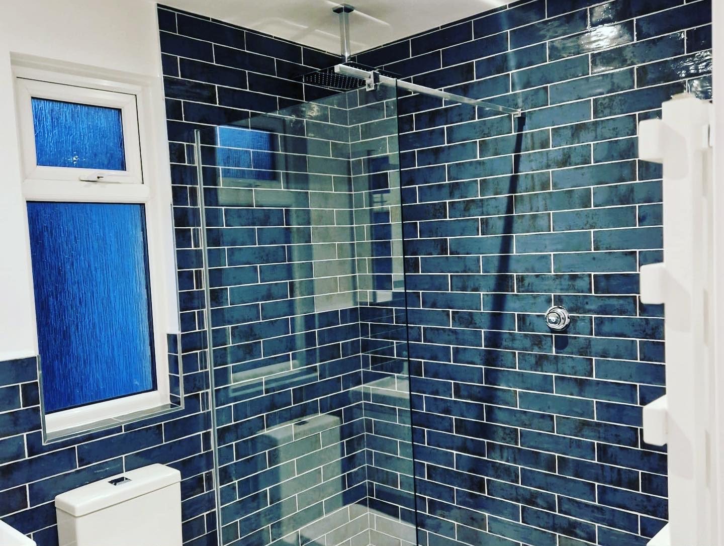 Shower area tiled in teal brick-bond metro tiles with a rainfall shower head
