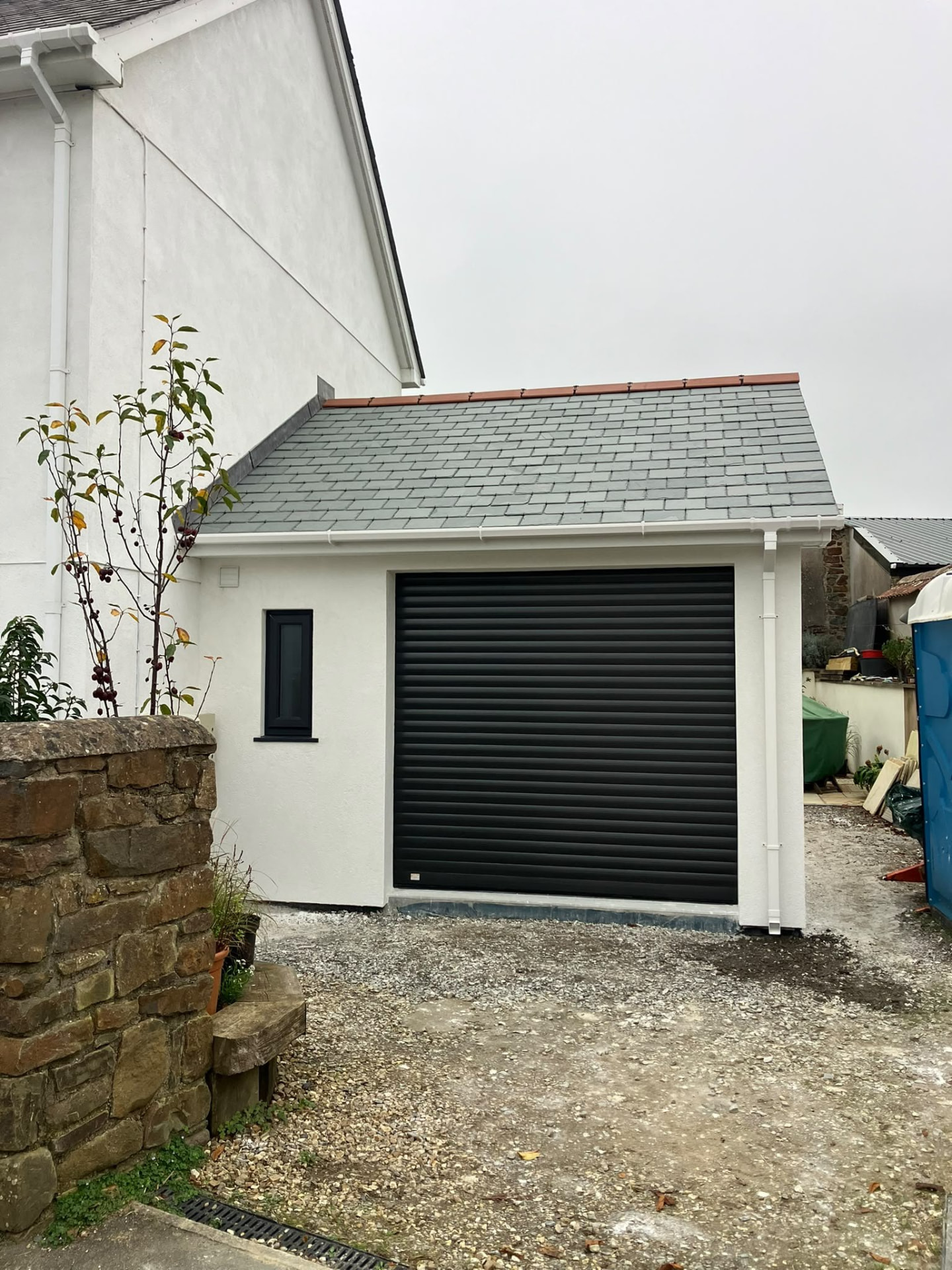 Rendered outbuilding with a roller door and a slate roof built for a private client