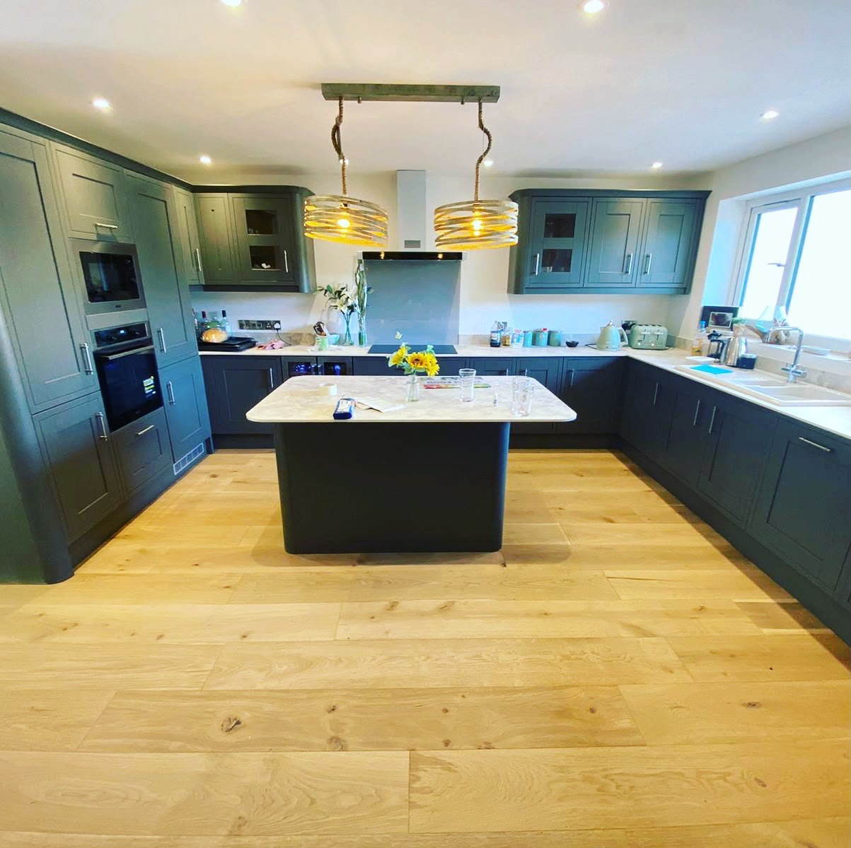 Dark green shaker kitchen with a central island and oak plank flooring