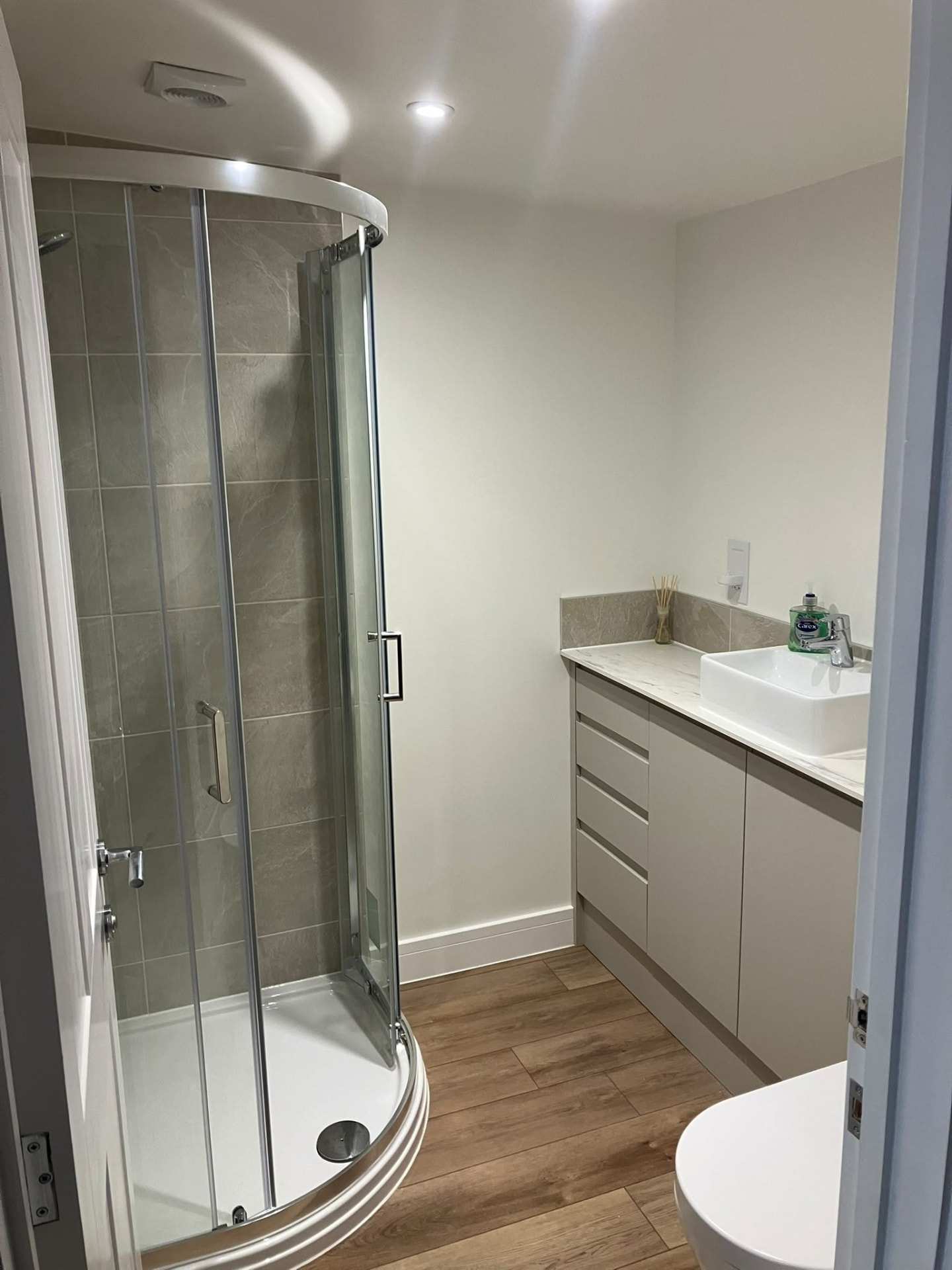 Bathroom installation in North Devon with a curved glass shower enclosure, tiled walls and a fitted vanity unit