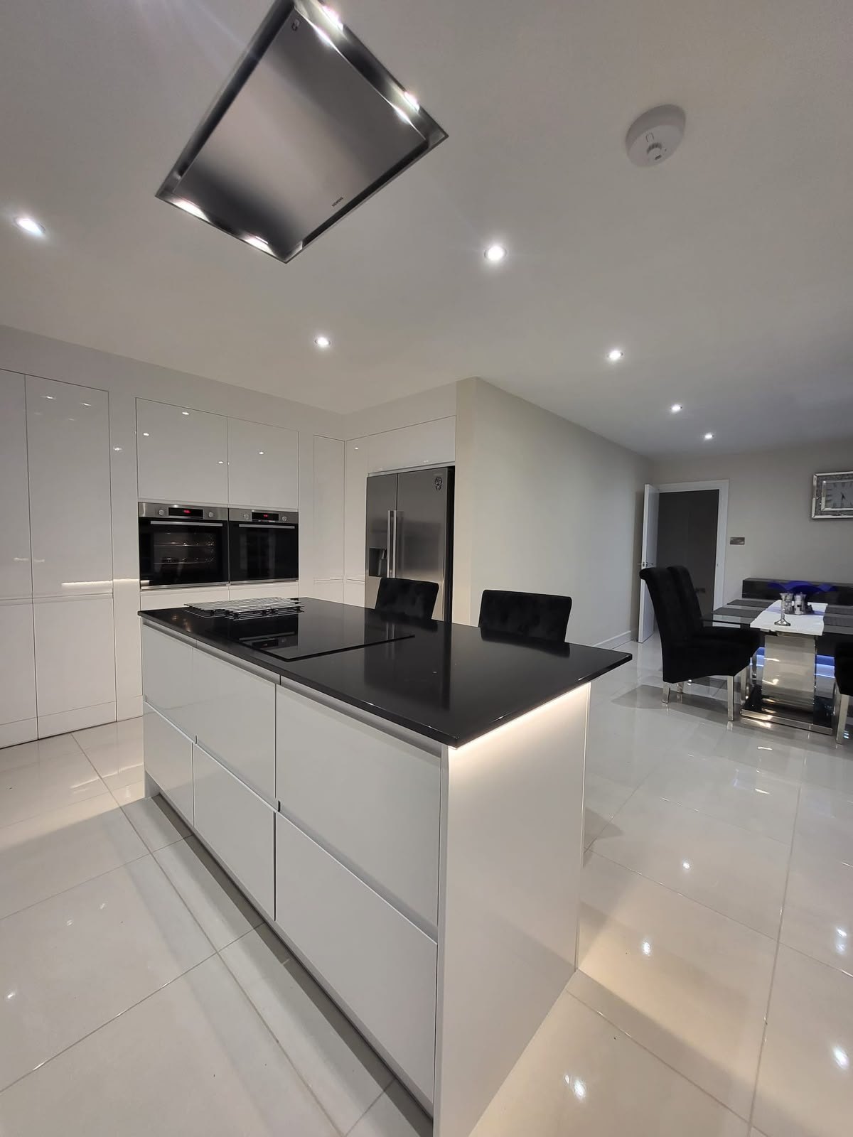 Handleless white kitchen with a black granite island worktop and ceiling extractor
