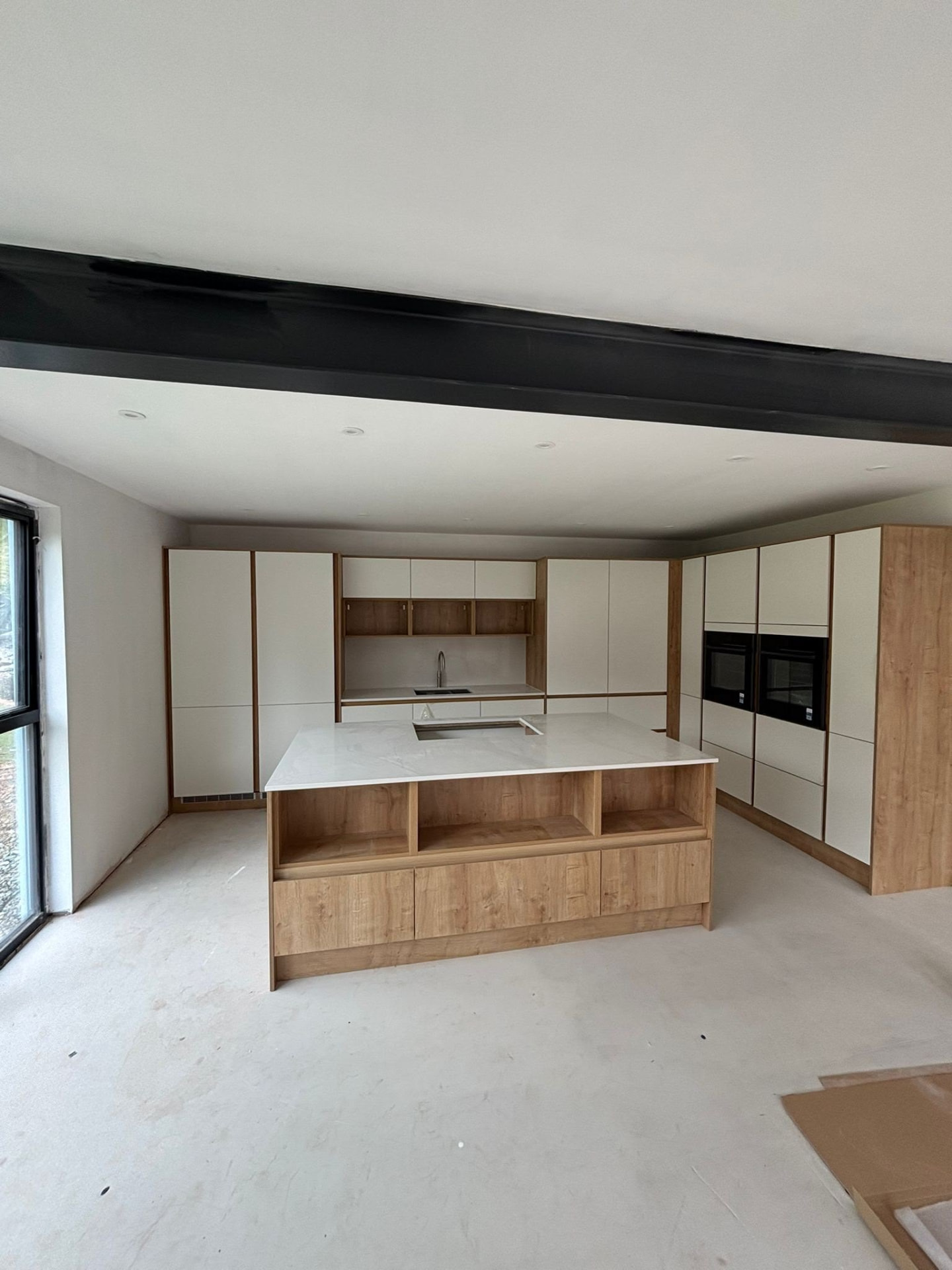 Renovated open-plan kitchen with handleless cream units, an oak island and an exposed steel beam across the ceiling