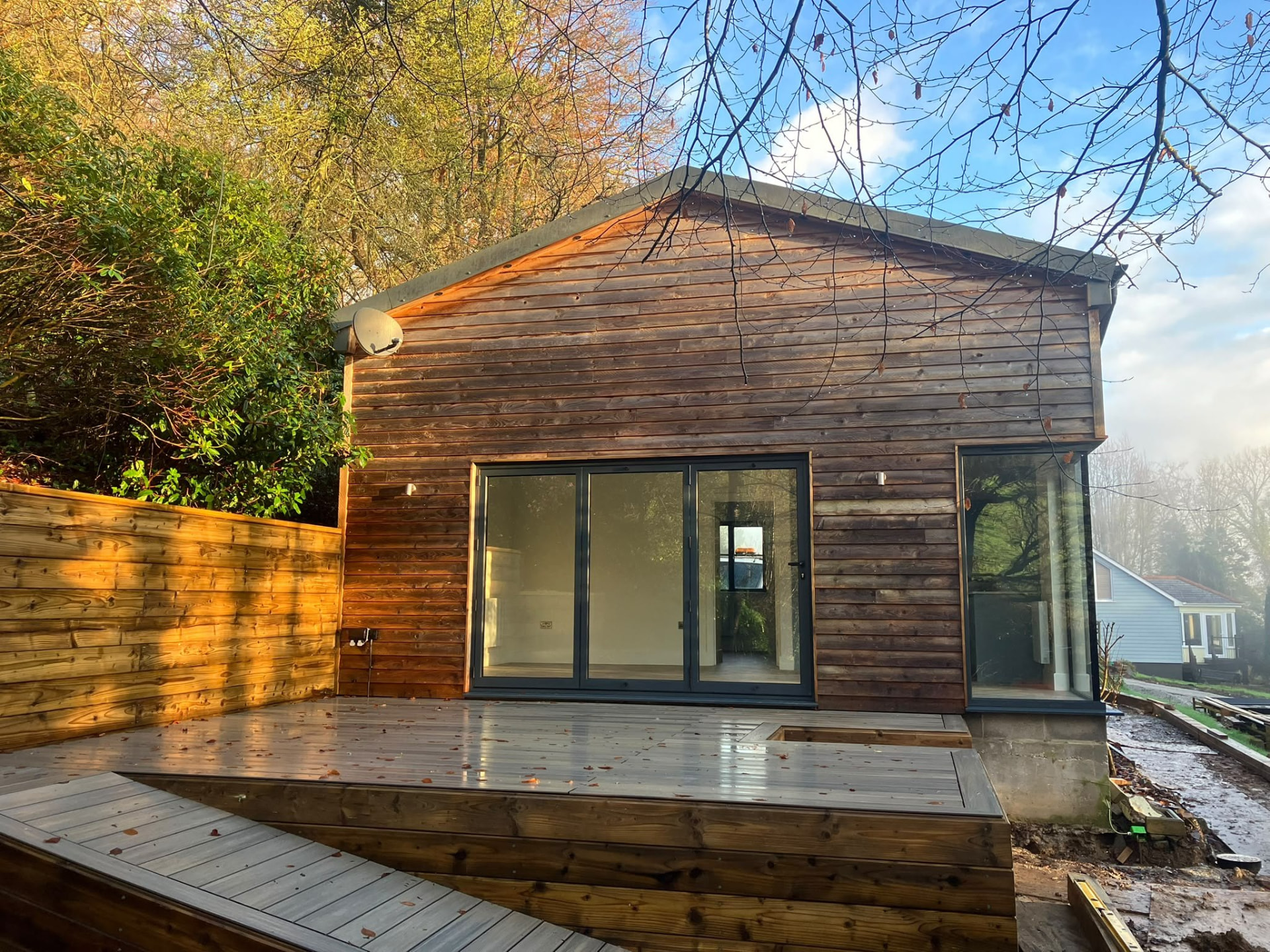 Timber-clad extension and deck with full-height glazing photographed at sunset