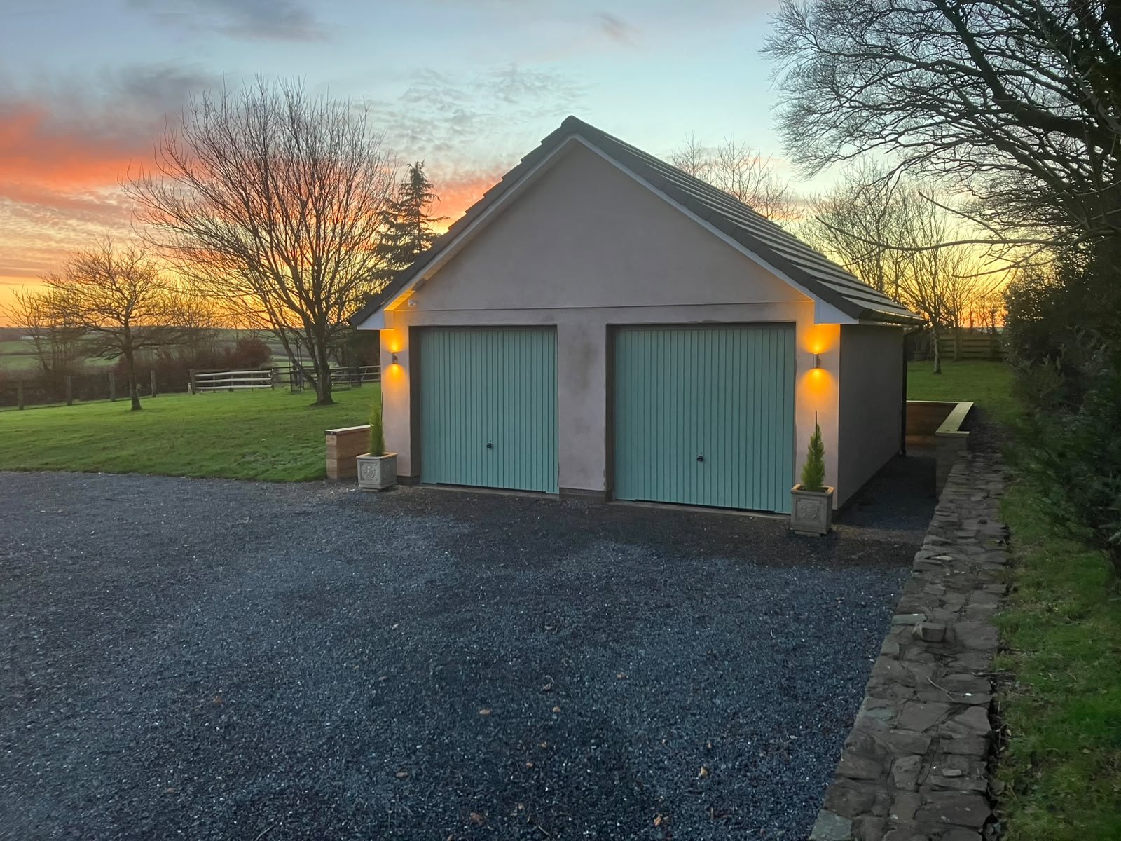 Detached double garage with timber doors and outdoor lighting at dusk