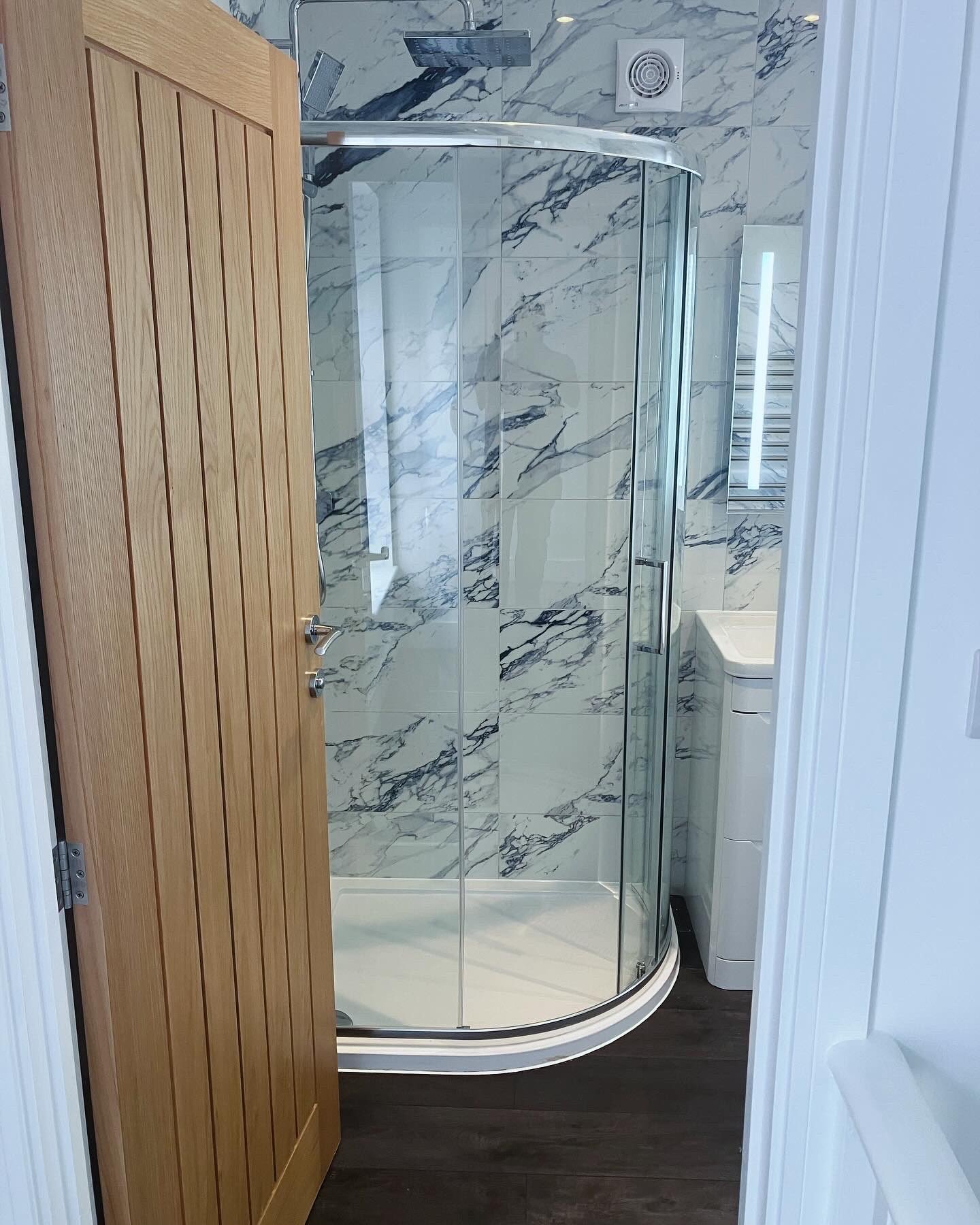 Marble-effect tiled bathroom with a curved glass shower cubicle, viewed from the landing doorway