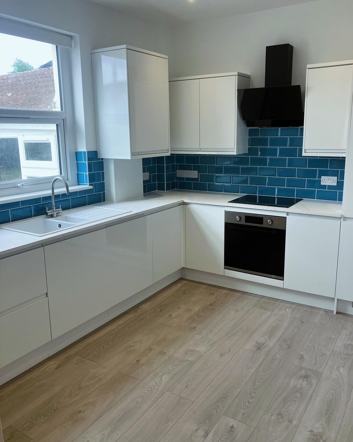 White gloss kitchen with a teal metro tile splashback and wood-effect flooring