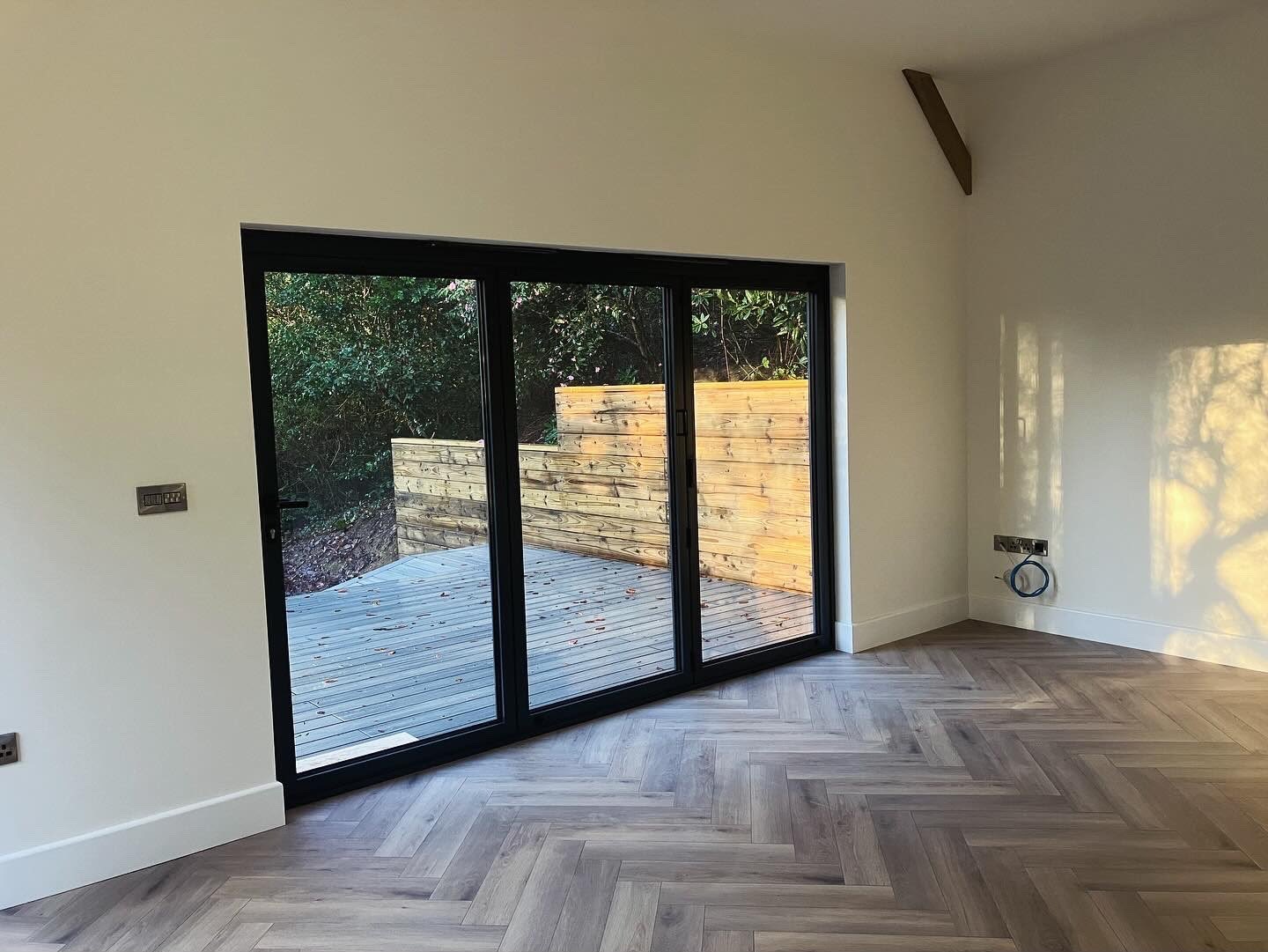 Open bi-fold doors in a new extension with herringbone timber flooring looking out to the garden