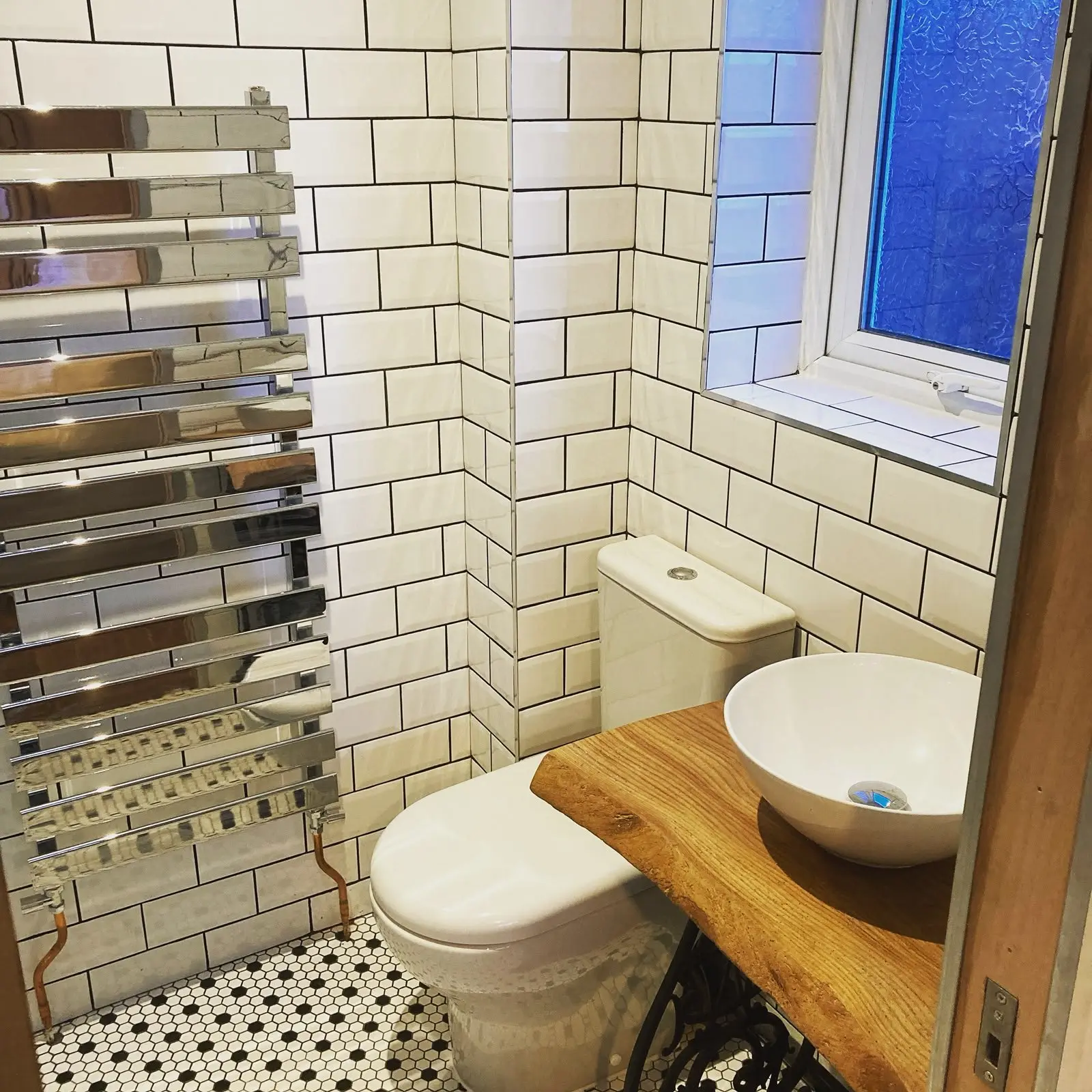 Cloakroom finished in white metro tiling with a live-edge timber vanity top, bowl basin and chrome towel rail